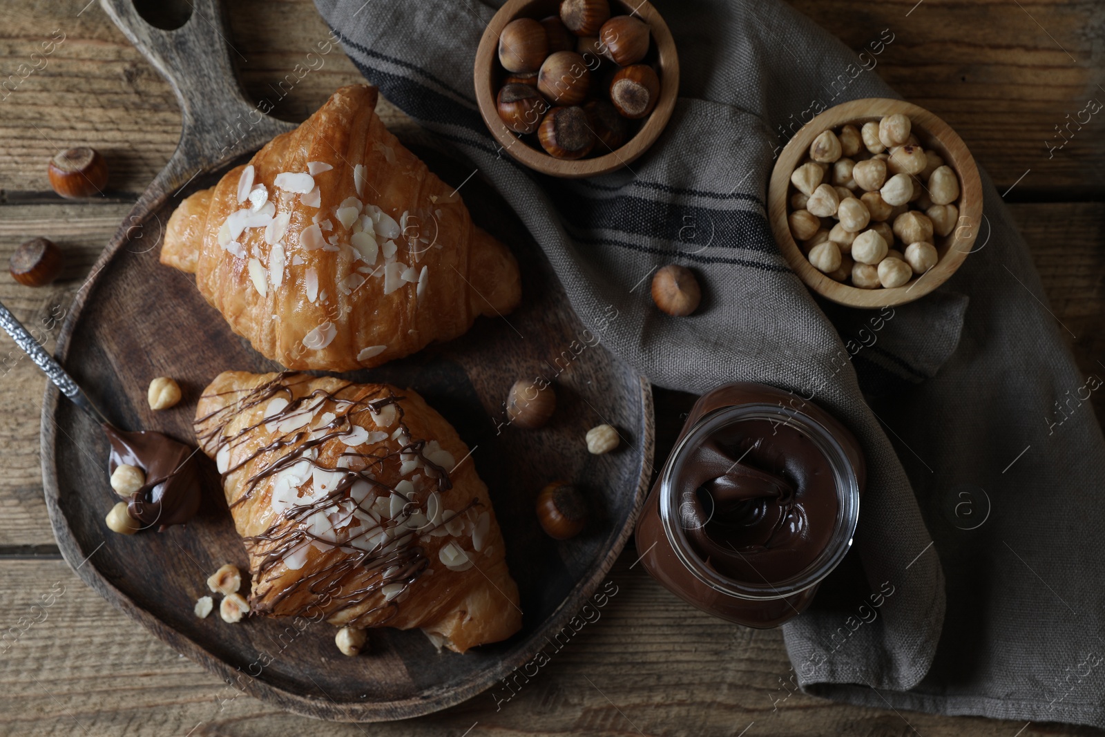 Photo of Delicious croissants with chocolate and nuts on wooden table, flat lay