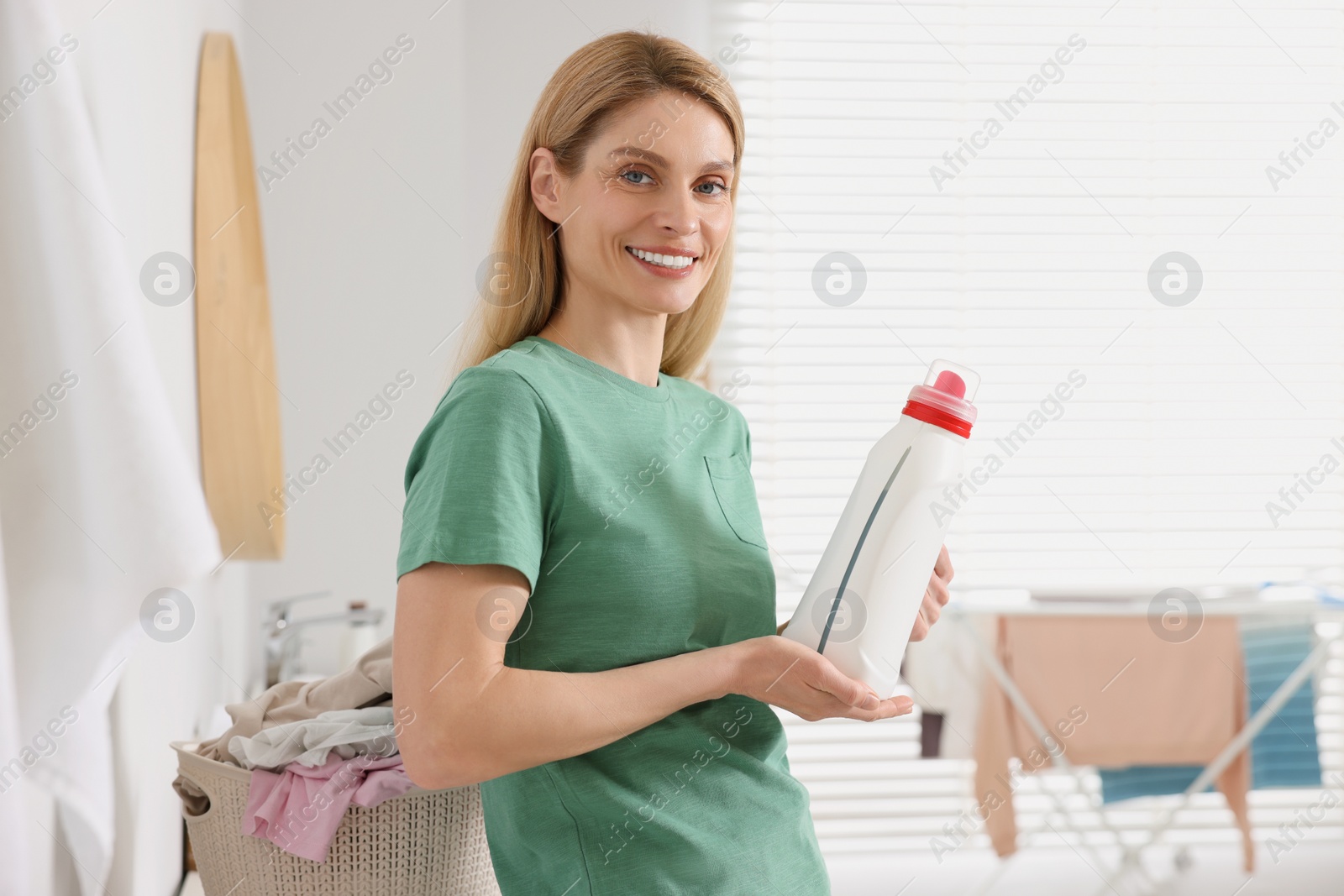 Photo of Beautiful woman holding fabric softener in bathroom
