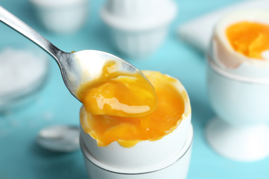 Eating soft boiled chicken egg with spoon at light blue table, closeup