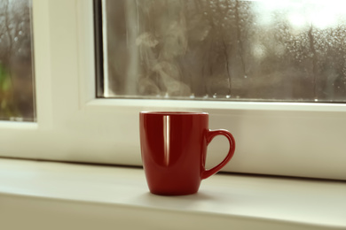 Cup of hot drink near window on rainy day