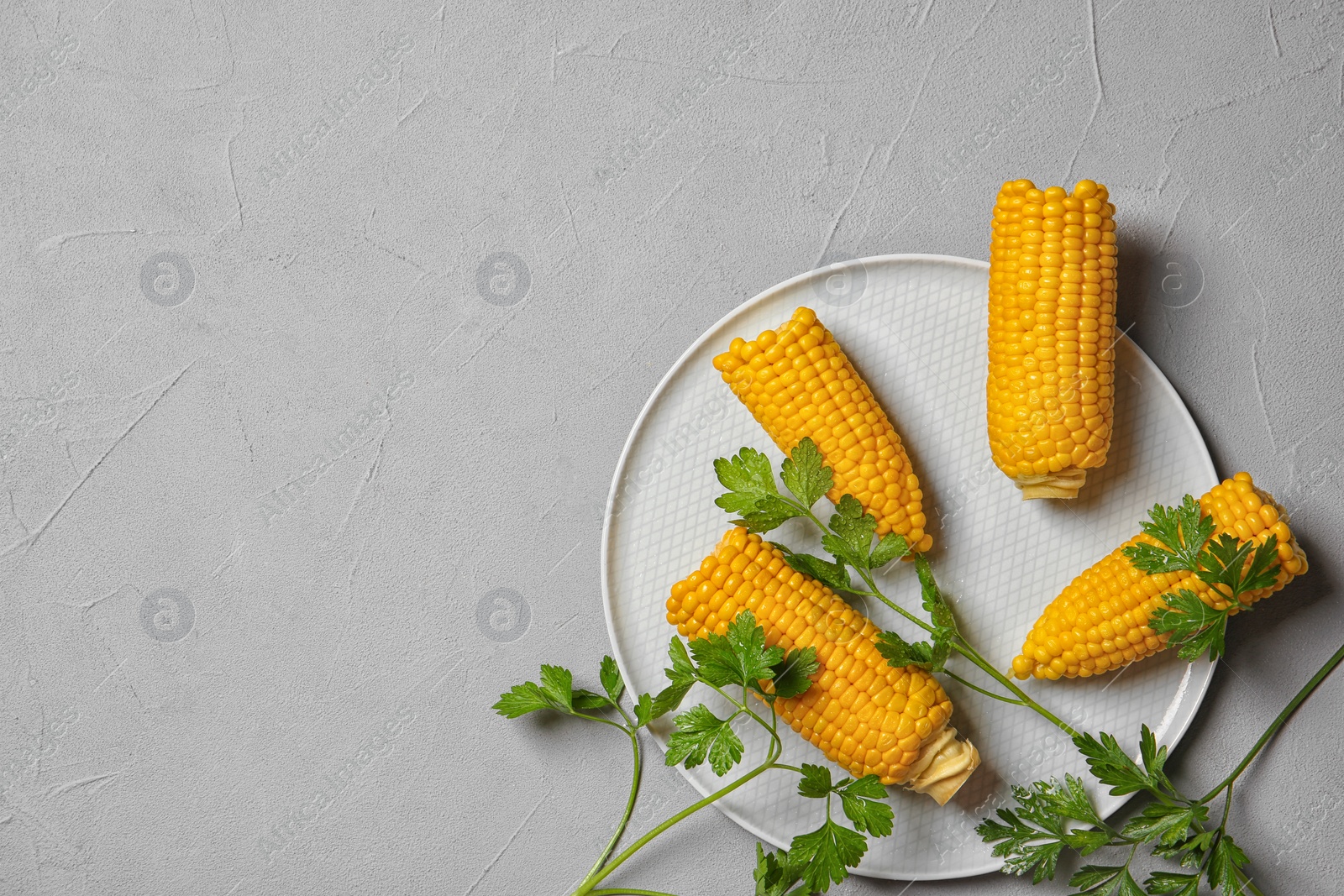 Photo of Plate with ripe corn cobs and parsley on grey background, top view. Space for text