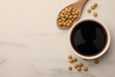 Soy sauce in bowl and soybeans on white marble table, flat lay. Space for text