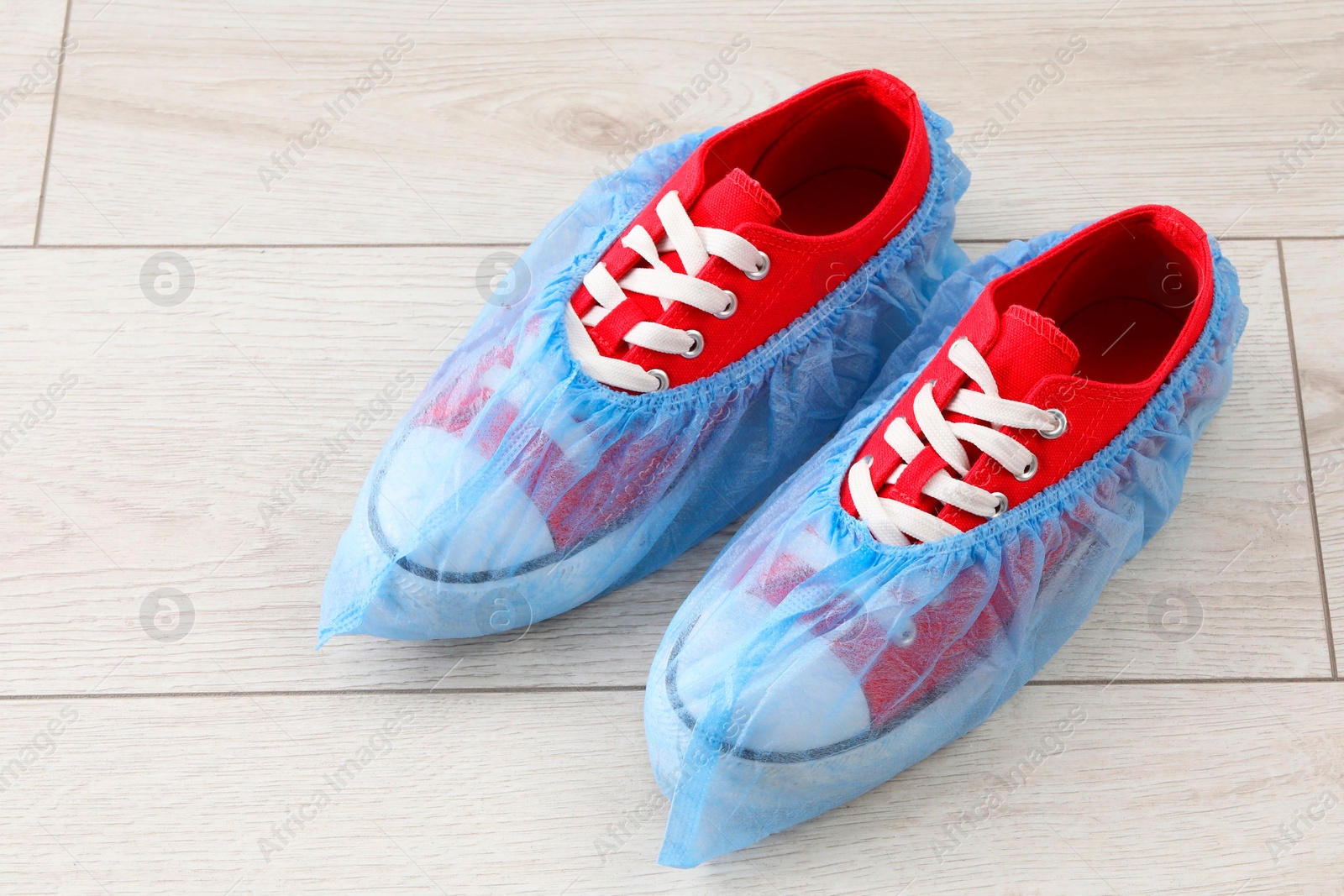 Photo of Sneakers in blue shoe covers on light wooden floor