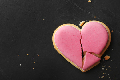 Photo of Broken heart shaped cookie on black table, top view with space for text. Relationship problems concept