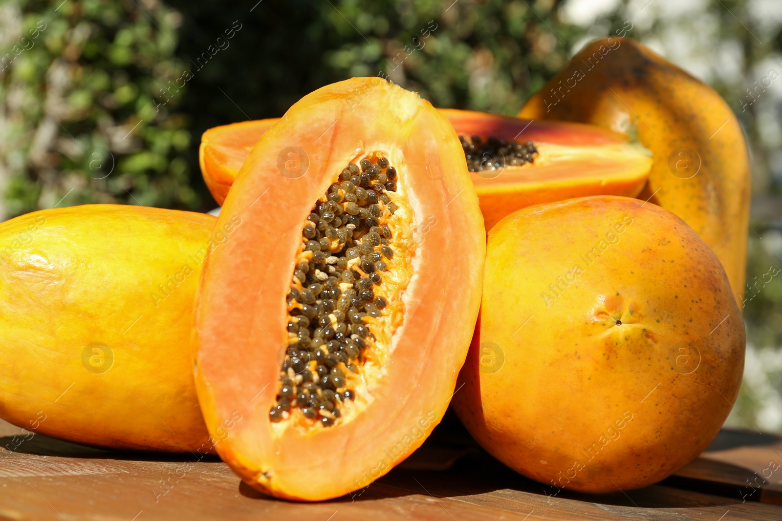 Photo of Fresh ripe cut and whole papaya fruits on wooden table outdoors, closeup