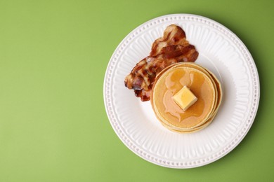 Photo of Delicious pancakes with butter, maple syrup and fried bacon on light green background, top view. Space for text
