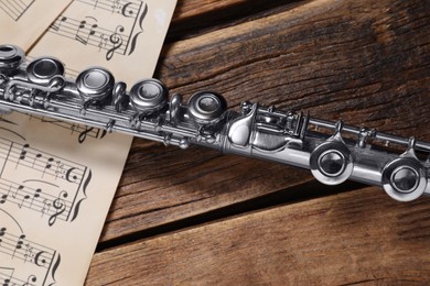 Photo of Sheets with musical notes and flute on wooden table, closeup