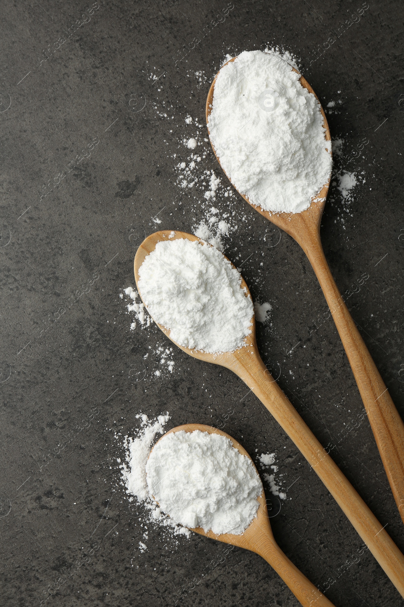 Photo of Baking powder in spoons on grey textured table, flat lay