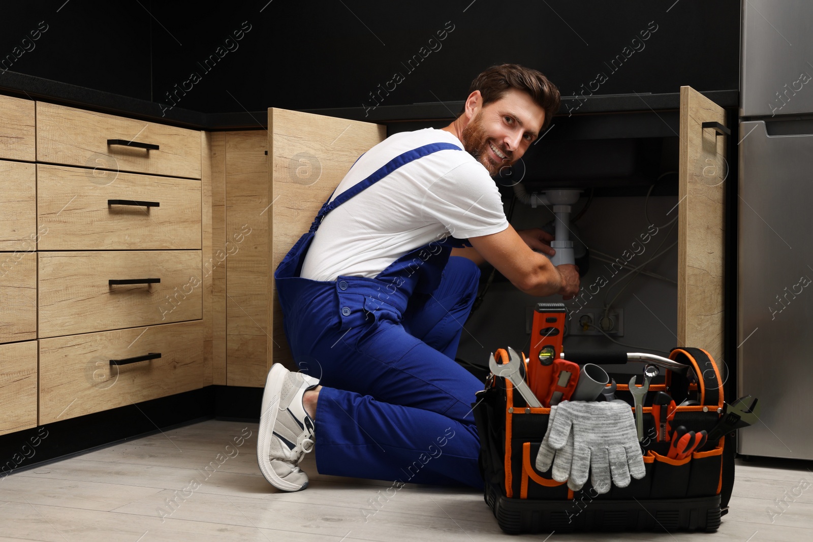 Photo of Professional plumber in uniform fixing sink indoors