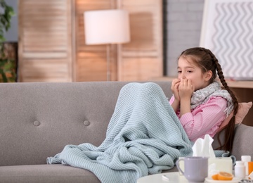 Little girl with tissue suffering from cold on sofa at home