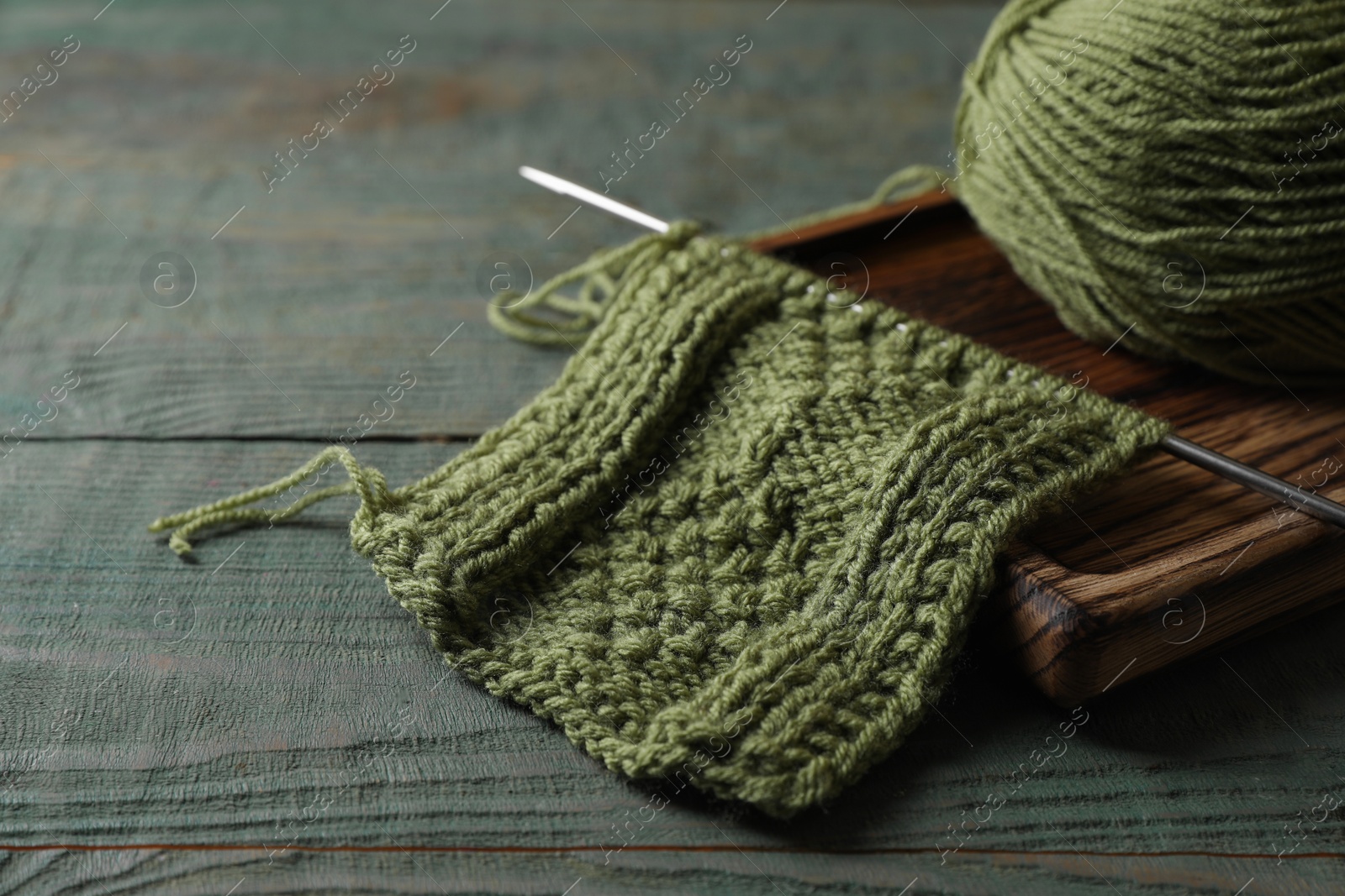 Photo of Soft yarn, knitting and metal needle on light blue wooden table, closeup