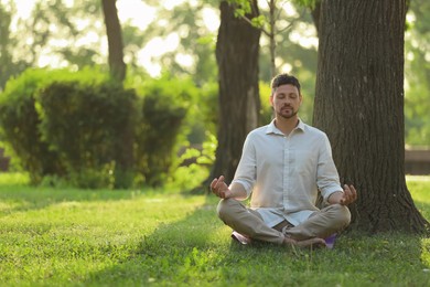 Photo of Man meditating in park on sunny summer day. Space for text