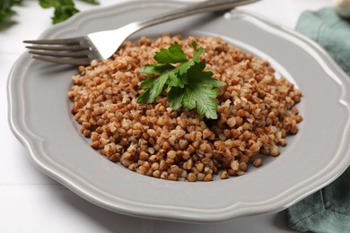 Tasty buckwheat with fresh parsley and fork on white table, closeup