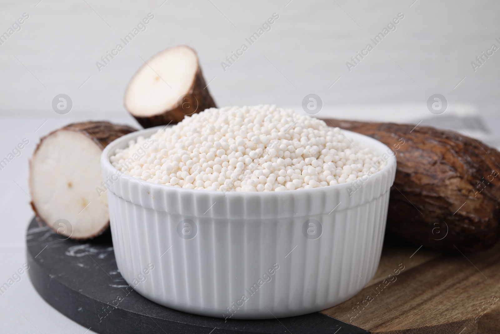 Photo of Tapioca pearls in bowl and cassava roots on table, closeup