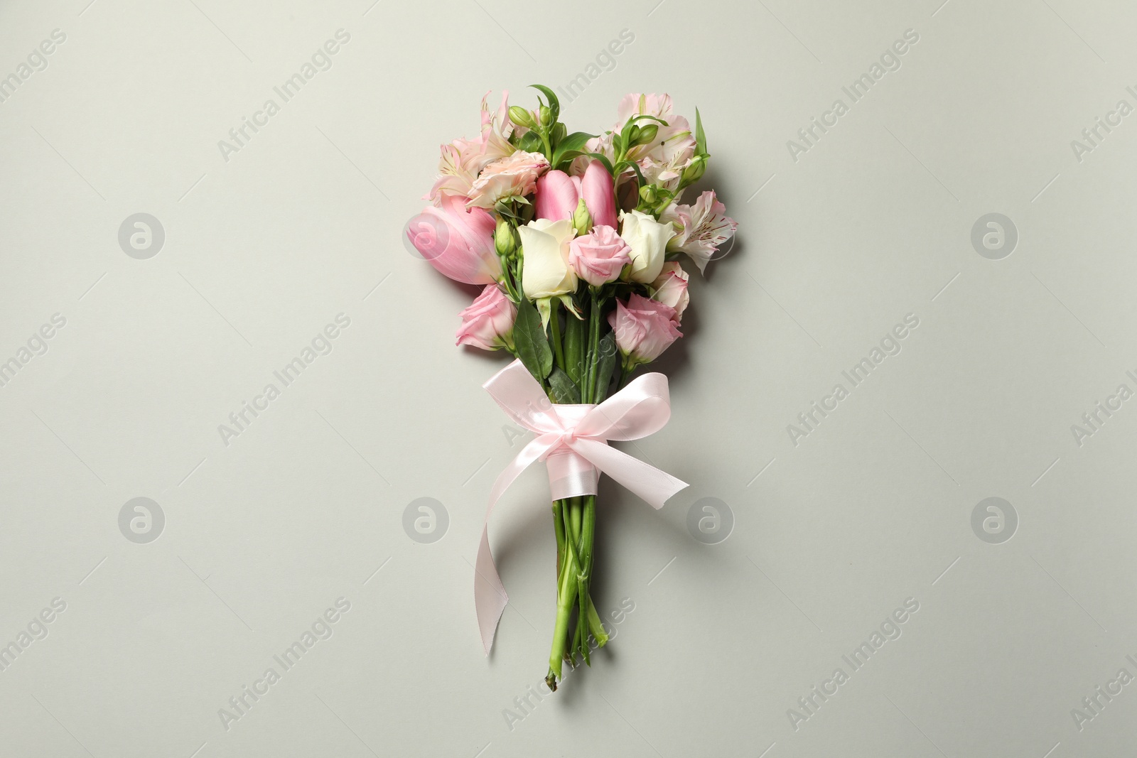 Photo of Happy Mother's Day. Bouquet of beautiful flowers tied with pink ribbon on light grey background, top view