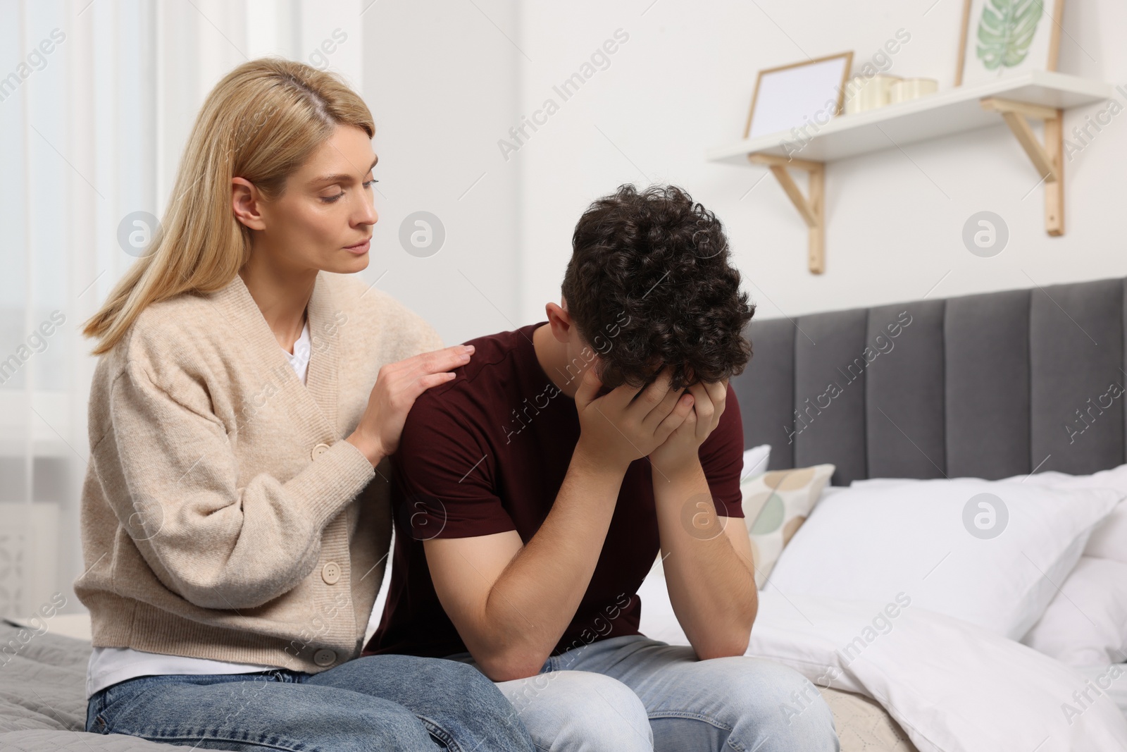 Photo of Mother consoling her upset son in bedroom, space for text. Teenager problems