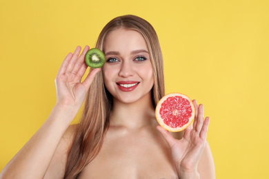 Photo of Young woman with cut kiwi and grapefruit on yellow background. Vitamin rich food