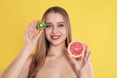 Young woman with cut kiwi and grapefruit on yellow background. Vitamin rich food