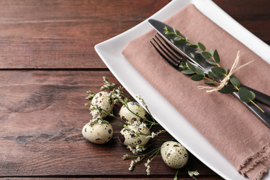 Festive Easter table setting with quail eggs and floral decor on wooden background, closeup