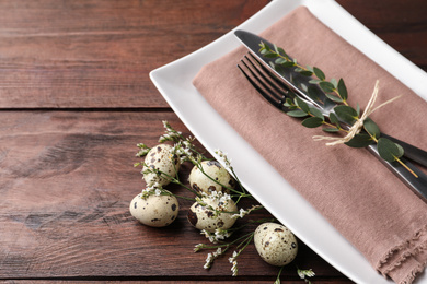 Photo of Festive Easter table setting with quail eggs and floral decor on wooden background, closeup