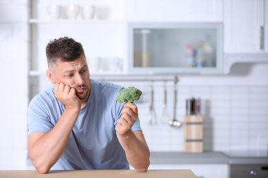 Photo of Portrait of unhappy man looking at broccoli in kitchen