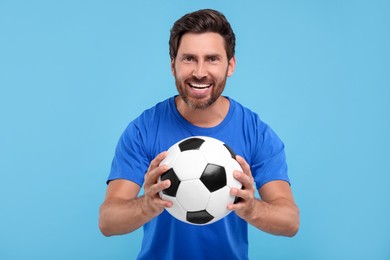 Photo of Emotional sports fan with soccer ball on light blue background