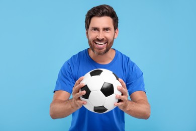 Emotional sports fan with soccer ball on light blue background