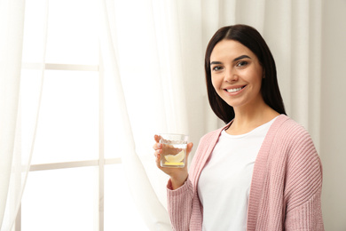 Photo of Beautiful young woman with tasty lemon water near window. Space for text