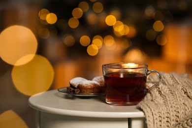 Photo of Cup of hot tea on white table against blurred lights, space for text. Cozy winter