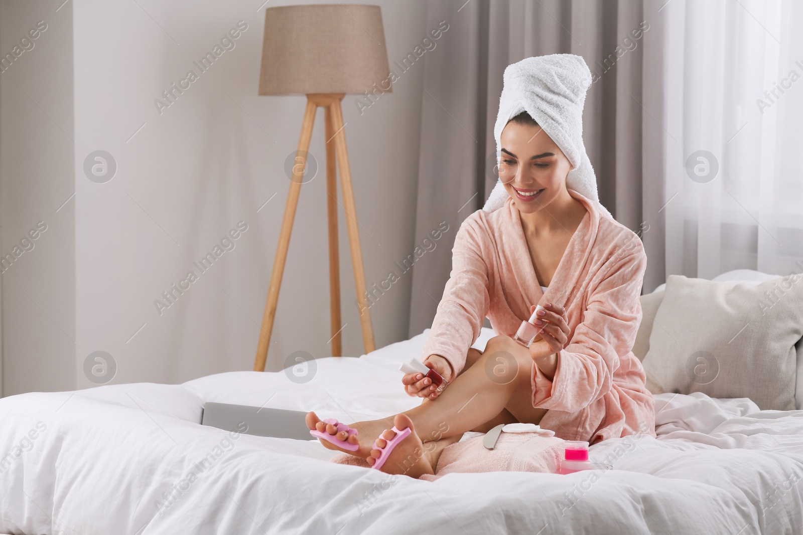 Photo of Beautiful young woman giving herself pedicure on bed at home