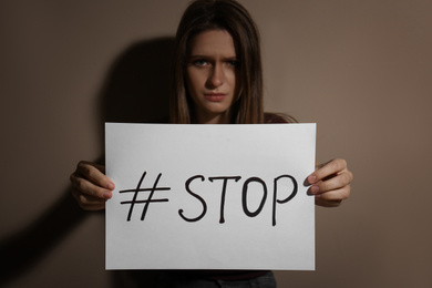 Photo of Abused young woman with hashtag STOP near beige wall. Domestic violence concept