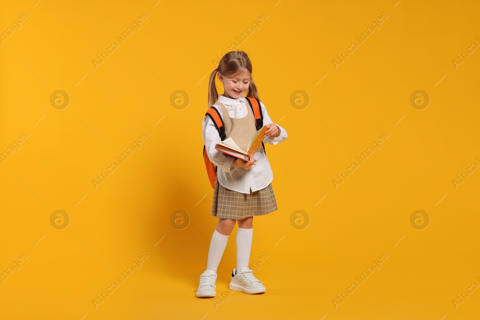 Photo of Happy schoolgirl with backpack and books on orange background