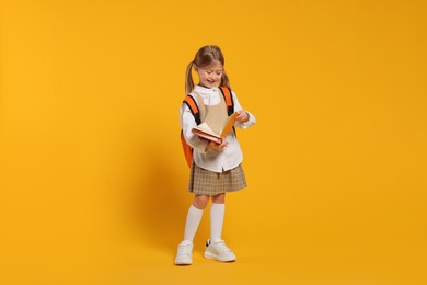 Happy schoolgirl with backpack and books on orange background