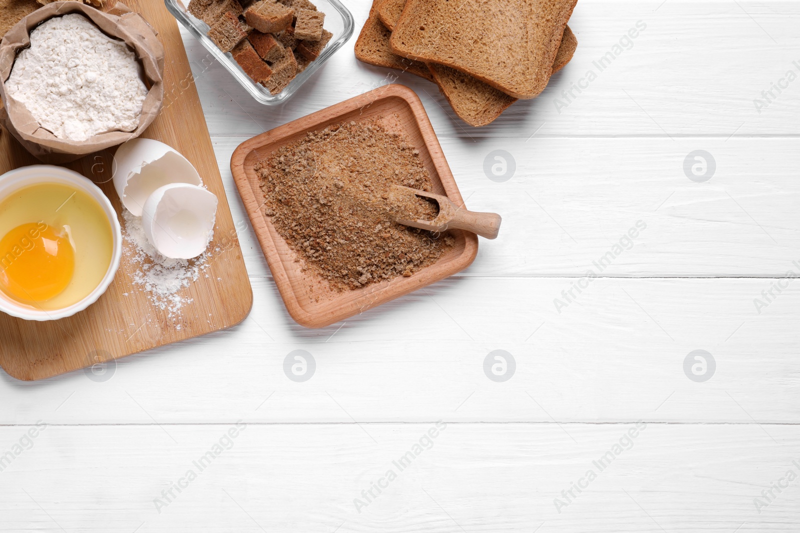 Photo of Fresh breadcrumbs, flour and egg on white wooden table, flat lay. Space for text