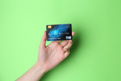 Photo of Woman holding credit card on light green background, closeup