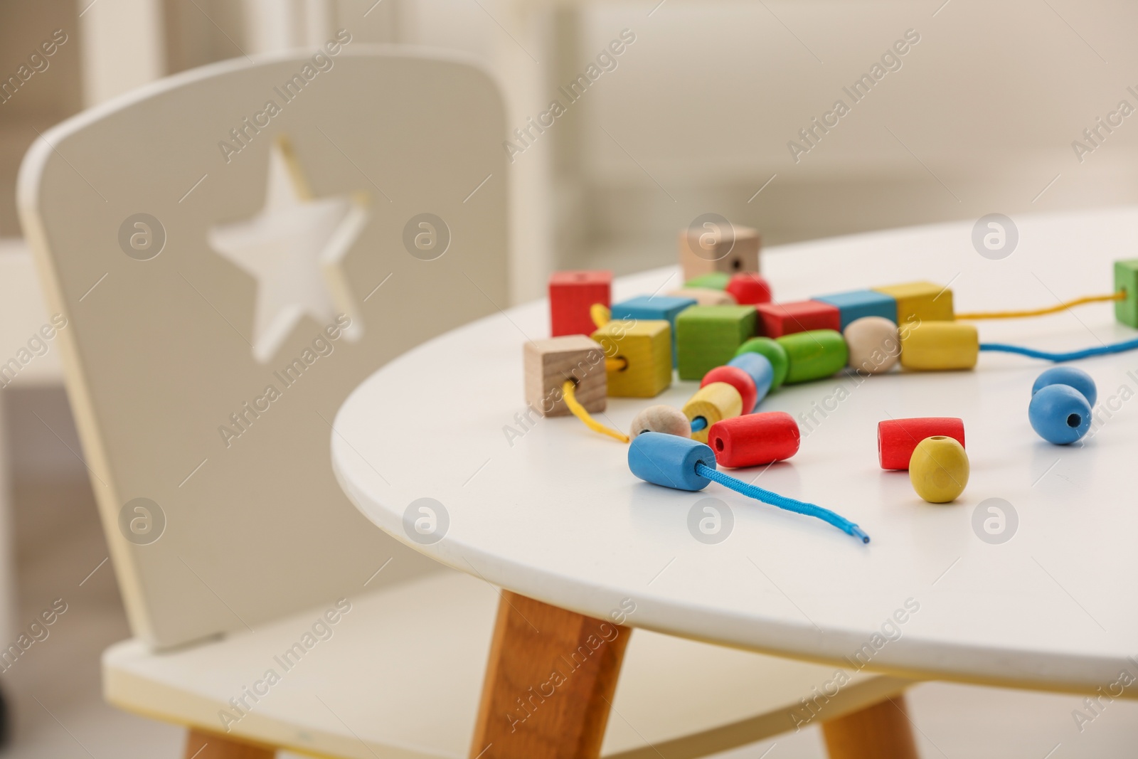 Photo of Wooden pieces and string for threading activity on white table indoors. Motor skills development