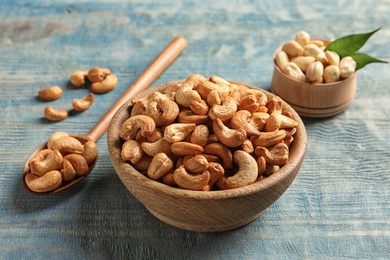 Photo of Tasty cashew nuts in bowl and spoon on wooden table