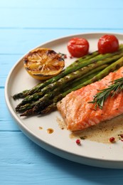 Tasty grilled salmon with tomatoes, asparagus and spices on light blue wooden table, closeup