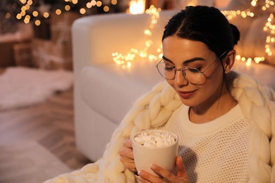 Young woman with cup of hot drink at home, space for text. Christmas celebration