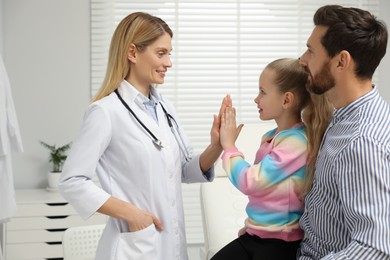 Photo of Happy father and daughter having appointment with doctor. Pediatrician and patient giving high five in clinic