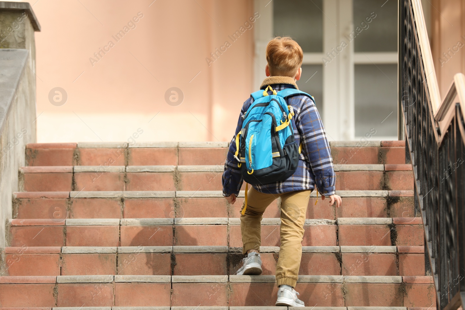 Photo of Little boy with backpack going up stairs to school, back view