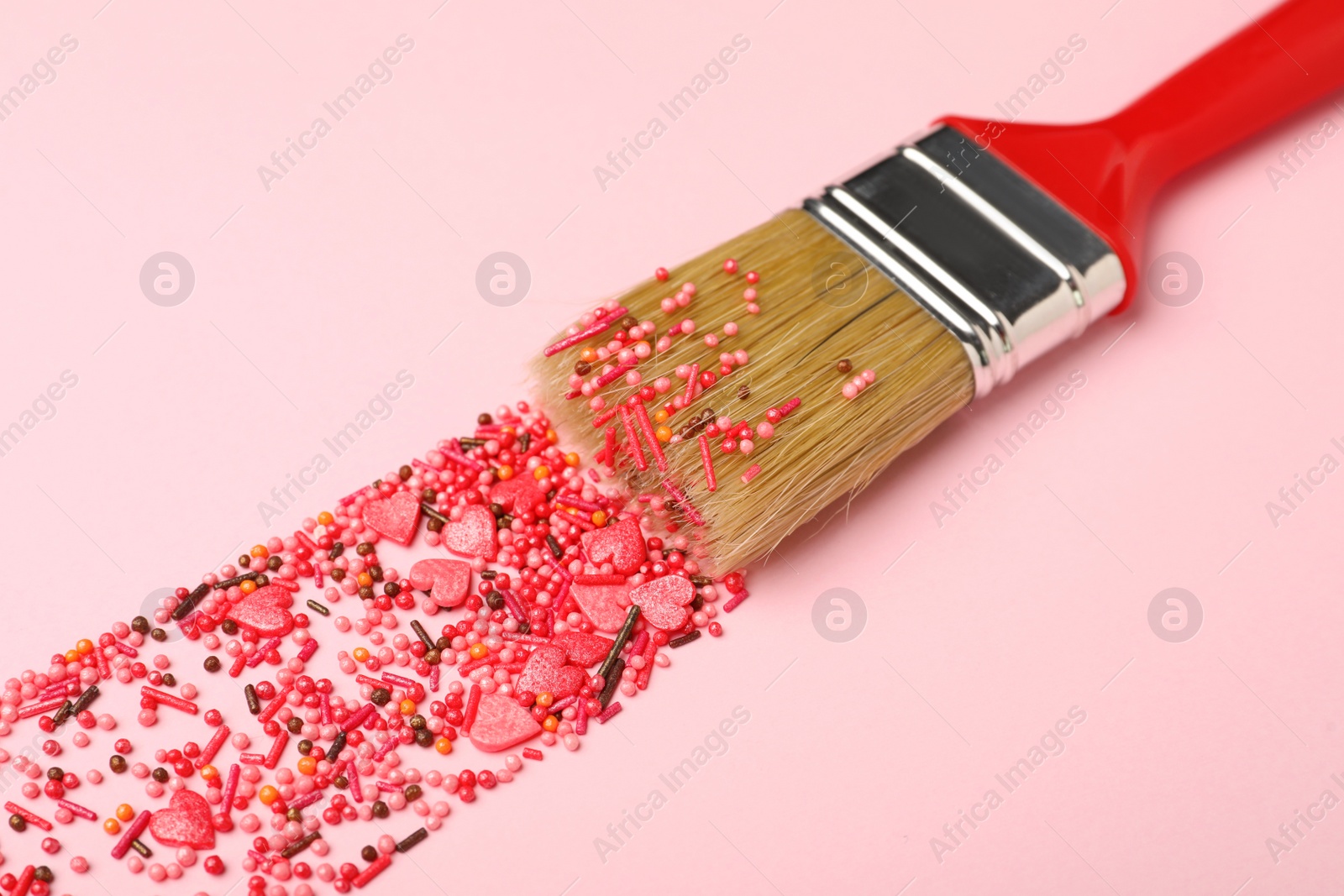 Photo of Brush painting with red sprinkles on pink background, closeup. Creative concept