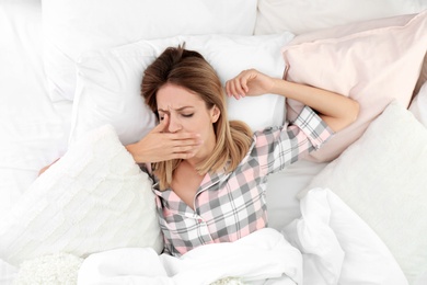 Photo of Young woman yawning in bed with pillows at home