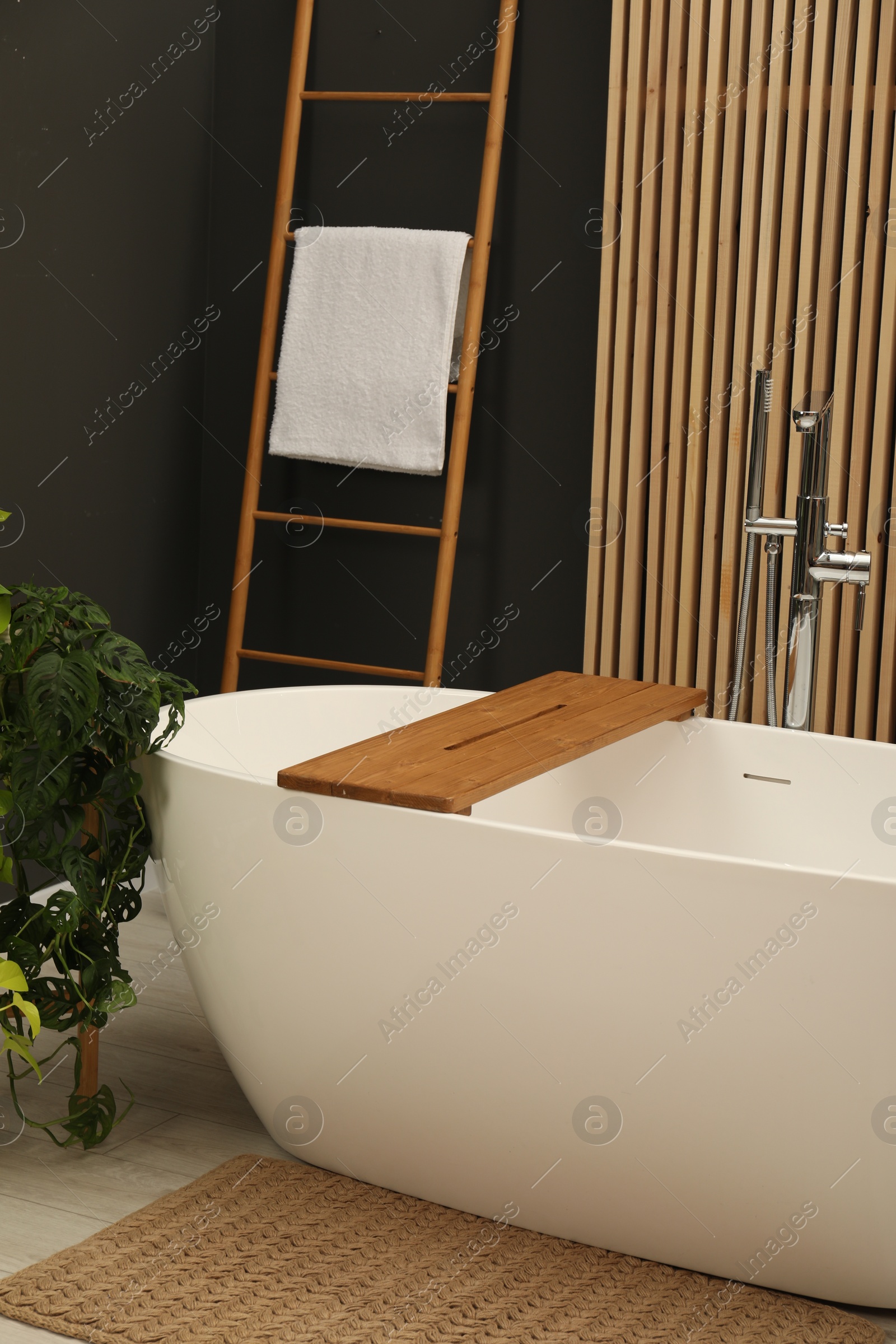 Photo of Spa day. Stylish bathroom interior with ceramic tub and green houseplant