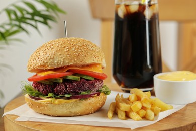 Photo of Tasty vegetarian burger served with french fries and soda drink on wooden table, closeup