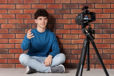 Photo of Smiling teenage blogger explaining something while streaming indoors