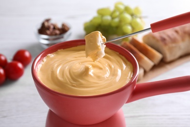 Dipping bread into pot with cheese fondue on table, closeup