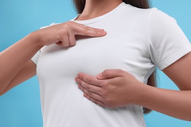 Photo of Woman doing breast self-examination on light blue background, closeup