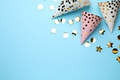 Bright party hats and shiny confetti on light blue background, flat lay. Space for text