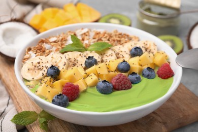 Tasty matcha smoothie bowl served with fresh fruits and oatmeal on table, closeup. Healthy breakfast